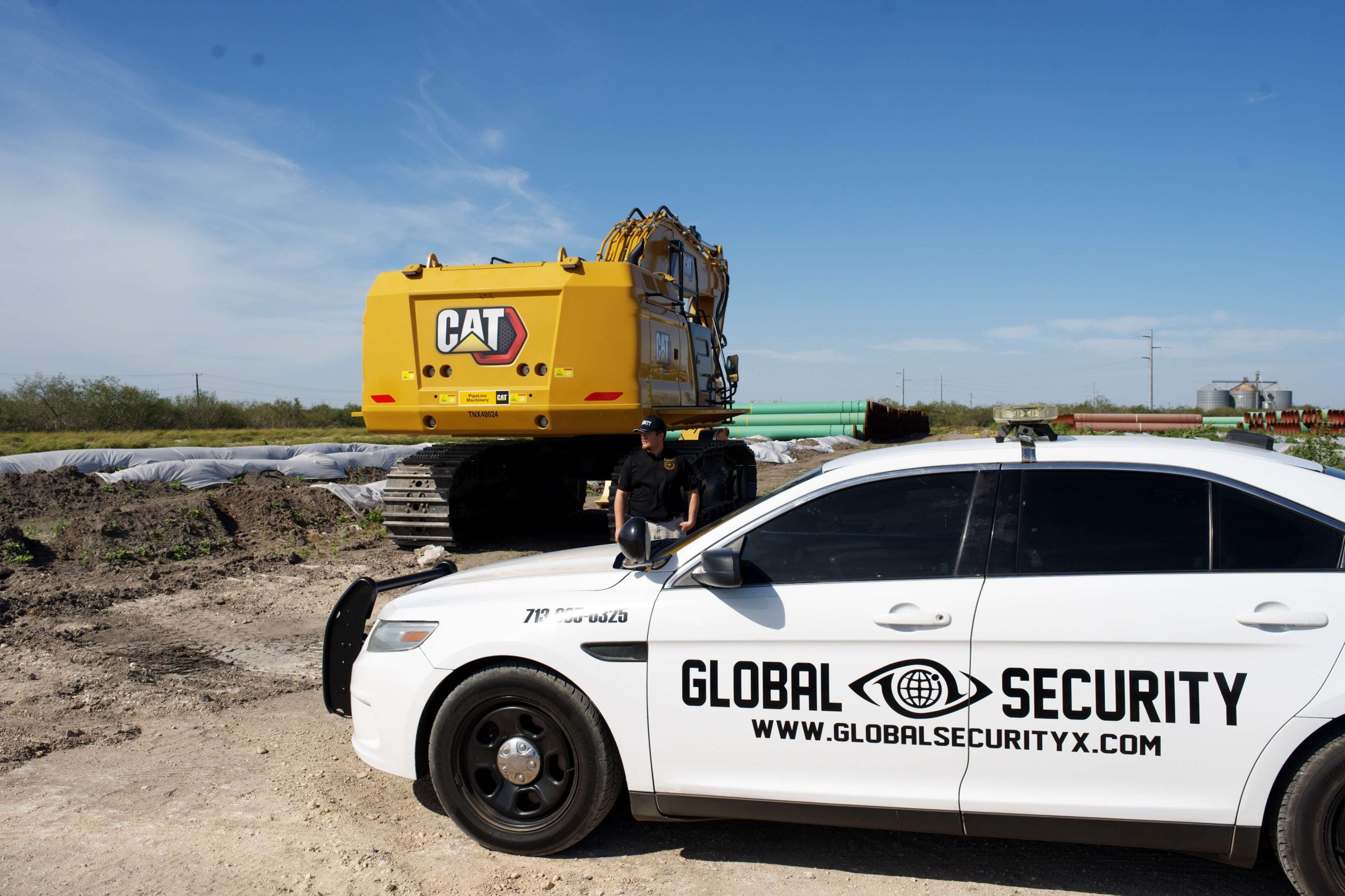 Security officer in front of marked Global Security vehicle, with a CAT excavator in the background, on a construction site in Midland, Texas.
