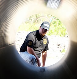 Security professional inspecting a surveillance detection area through a pipe, emphasizing Global Security's bug sweep services.