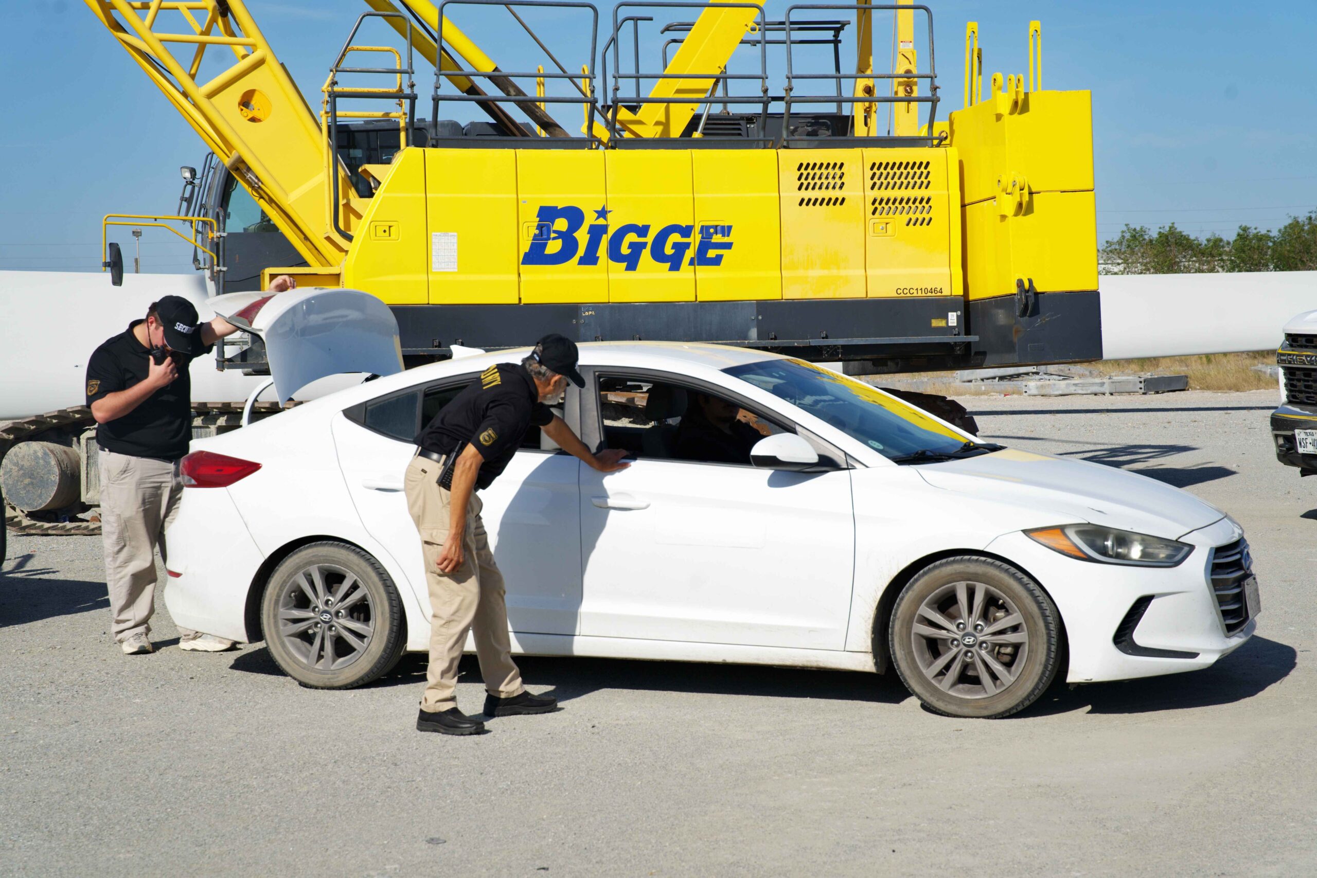 Security personnel inspecting vehicle at industrial site in Sulphur, Louisiana, with large yellow machinery in background, emphasizing professional security services.