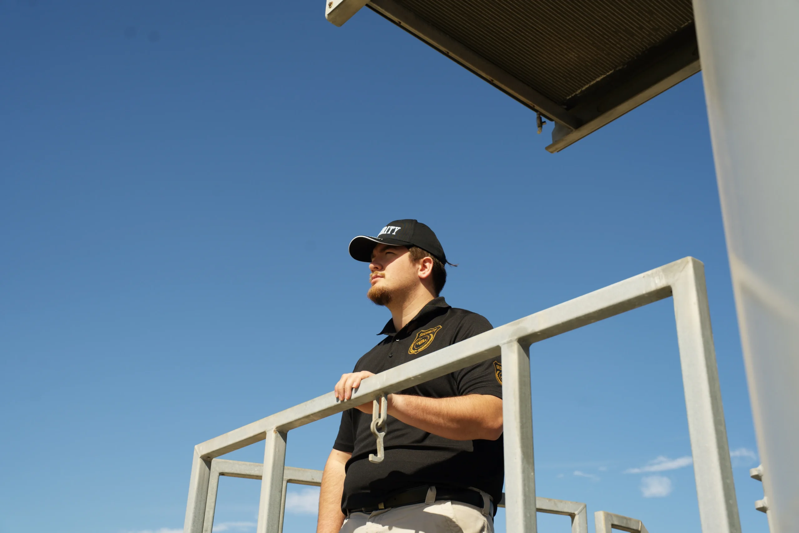 Security guard observing from a platform, wearing a uniform and cap, against a clear blue sky, emphasizing specialized security for Louisiana's oil and gas industry.