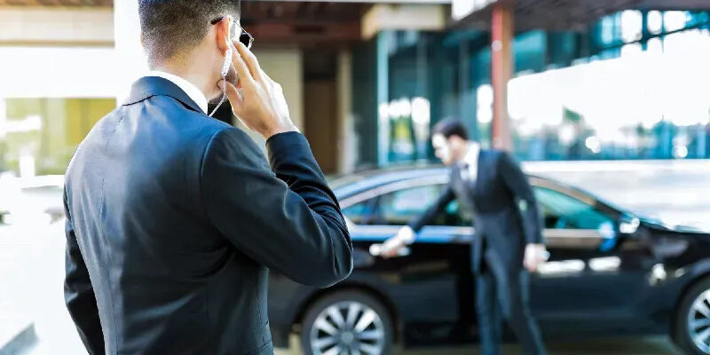 Man in a suit talking on the phone while another man opens a car door.