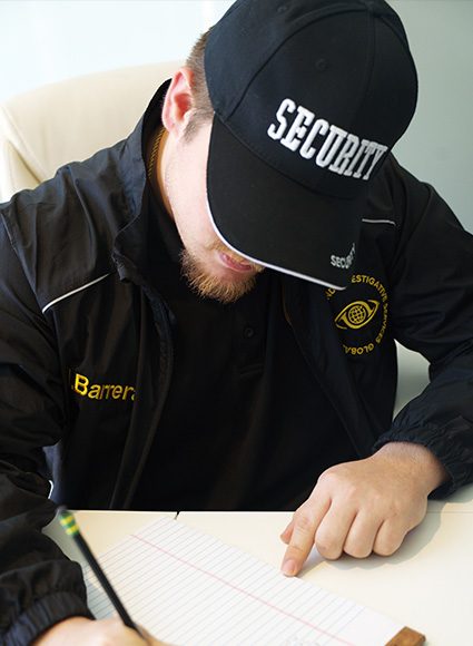 Security personnel writing notes, wearing a "SECURITY" cap and a jacket with "Barrera" embroidered, reflecting professional investigative services.