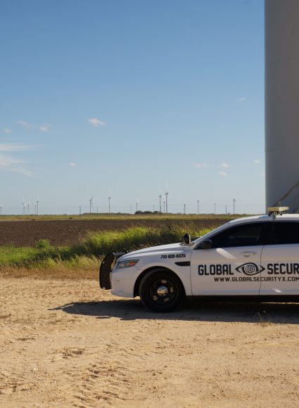 Global Security vehicle parked in industrial area with wind turbines in the background, representing specialized industrial security services in Louisiana.